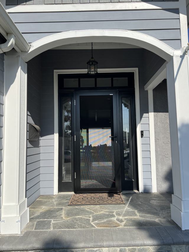 Black hinged security screen door with sidelights under an arched white porch on a gray-sided home