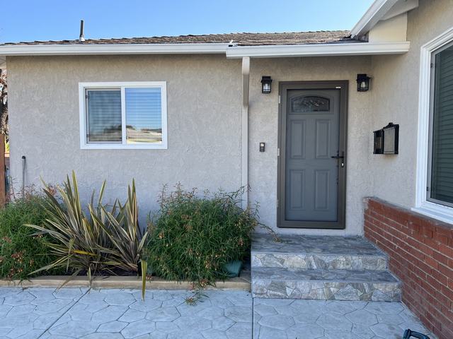 Gray hinged security screen door color-matched to the front door of a stucco home with stone steps