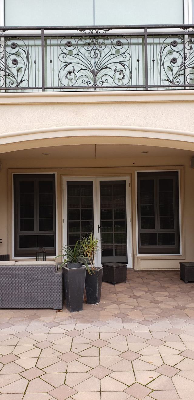 White French-door security screens under a balcony, opening onto a paved patio