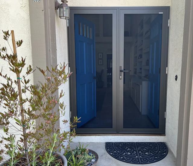 Bronze double security screen doors over blue front doors, with potted plants by the step