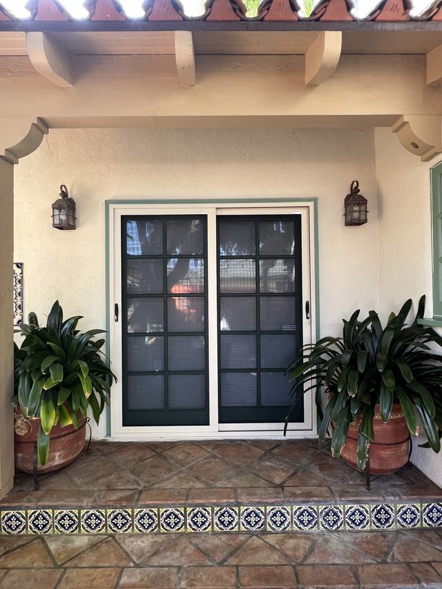 White sliding security screen door over divided-glass patio doors on a Spanish-style tiled porch