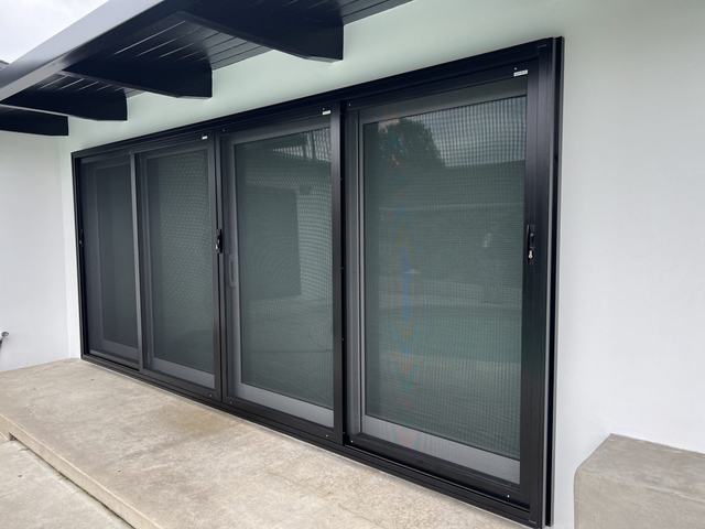 Black four-panel sliding security screen door on a white home with dark roof beams