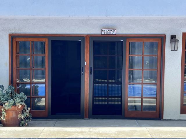 Black sliding security screen doors between wood-framed French windows on a poolside room