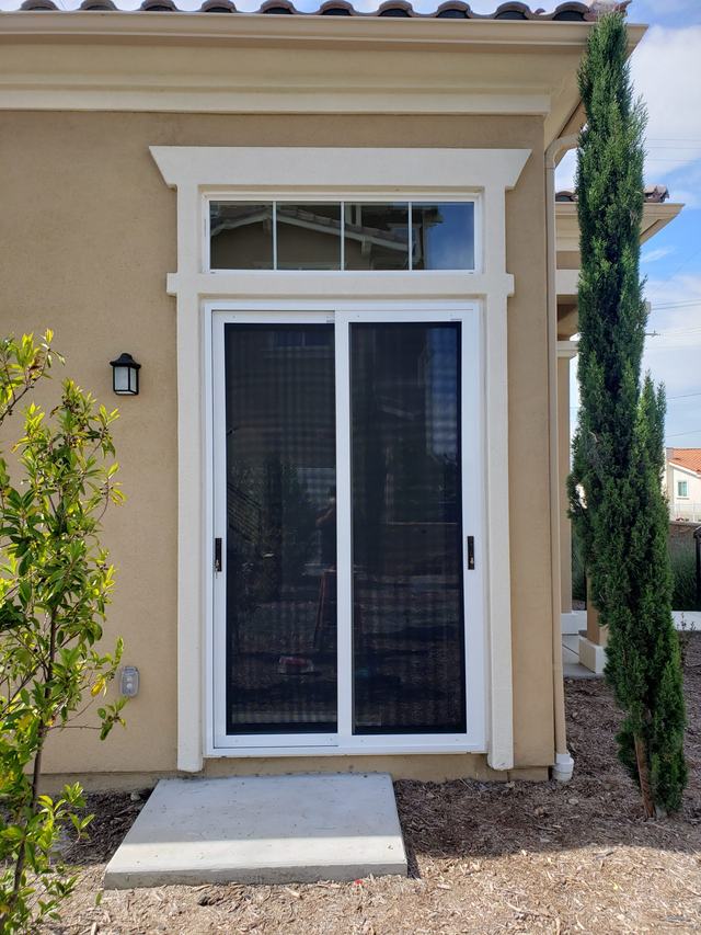 White sliding security screen door with a transom window above, on a tan stucco home