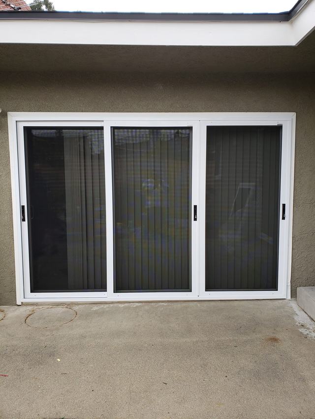 White three-panel sliding security screen door on a back patio