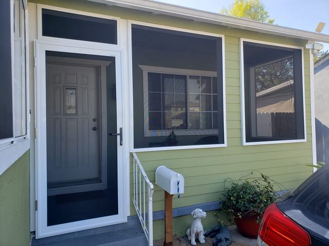 Green home with a white-framed hinged security screen door and fixed security screen panels around the porch