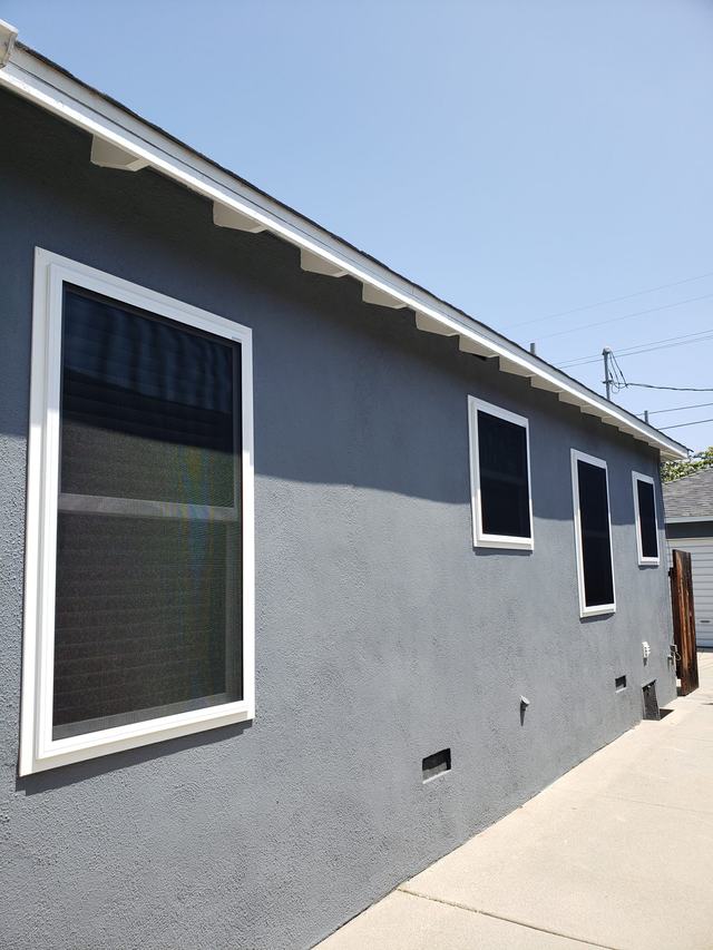 White-framed fixed security screens on four windows along the side of a gray stucco home