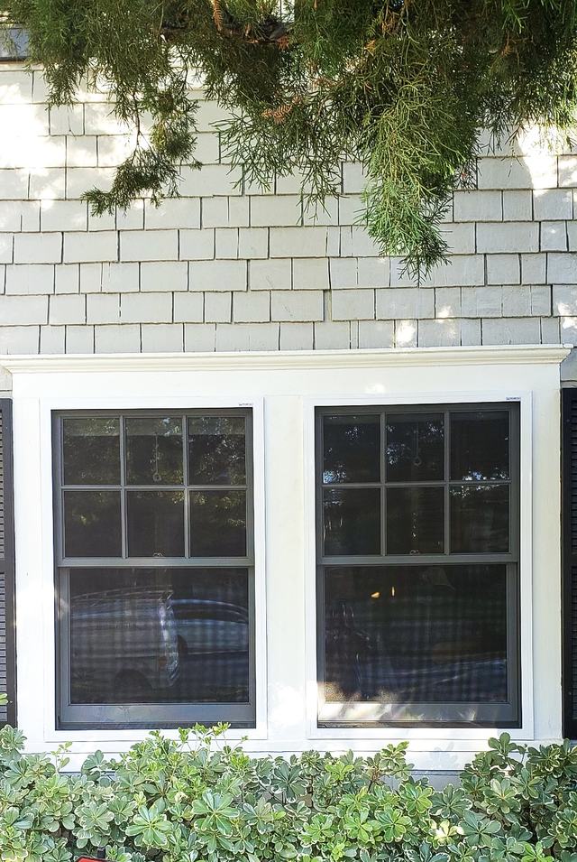 Two fixed security screens on double-hung windows of a white shingle home