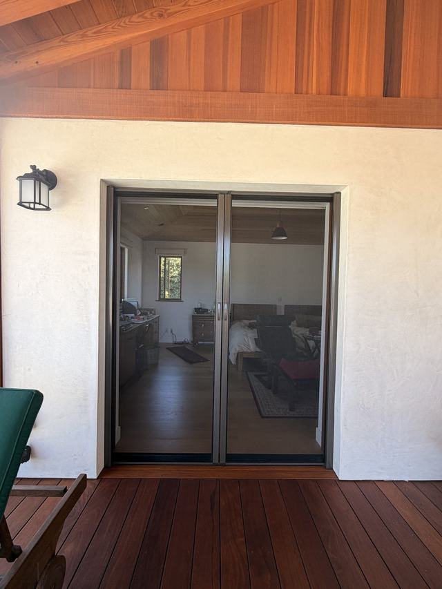 Double retractable screen closed across French doors that open onto a wood deck under a timber ceiling