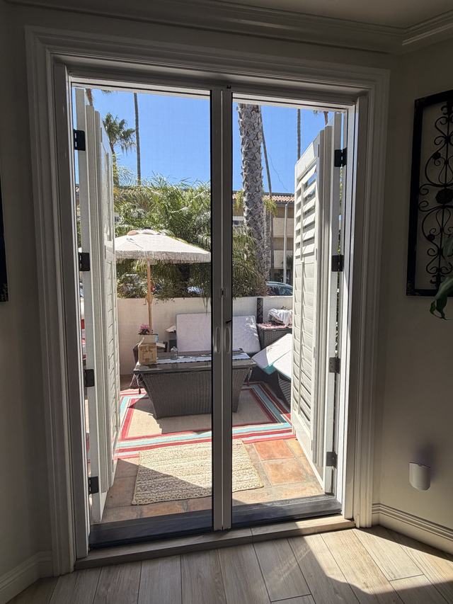 View from inside through a double retractable screen on French doors to a patio with palm trees