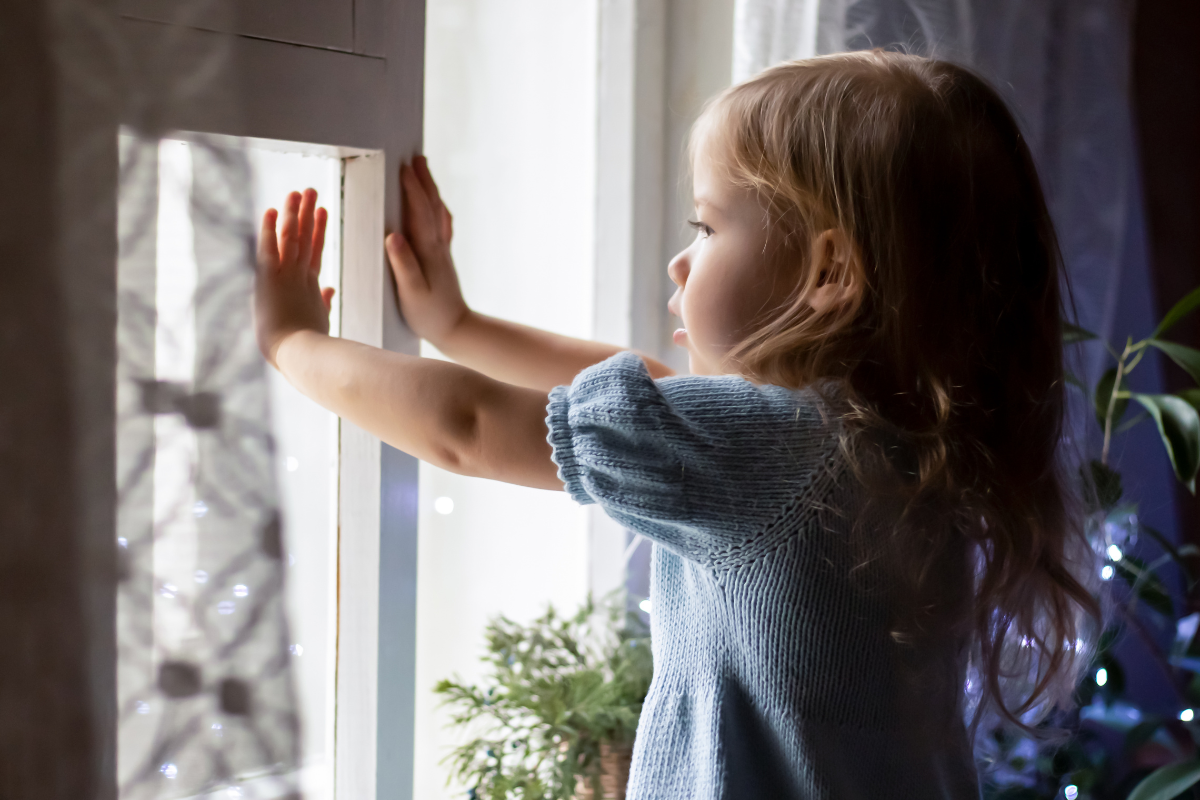 A young girl pressing her hands against a window glass in her home in Southern California.